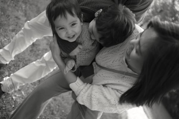 Toddler smiling up at the camera while his mother hugs him, black and white