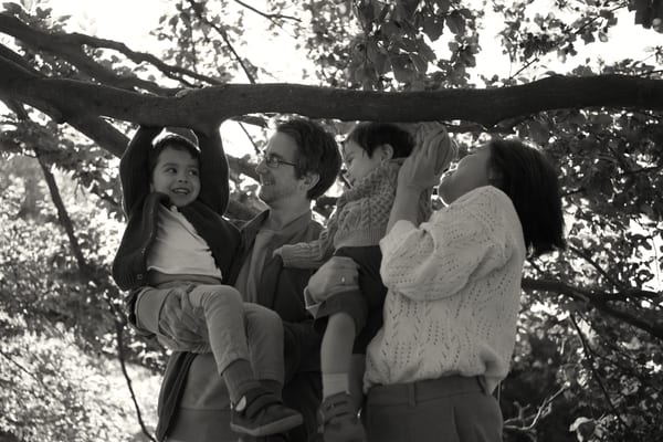 Parents lifting two boys up to hang from a low tree branch, black and white