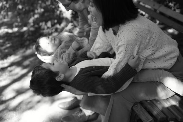 Boys leaning back over their mother's lap on a park bench, black and white