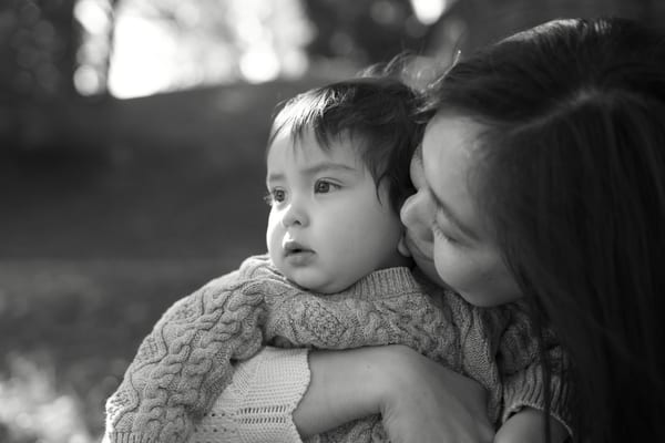 Mother holding her toddler close and kissing his cheek, black and white