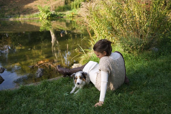 Woman lying on the grass by a pond, her dog stretched out next to her