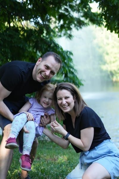 Parents crouching with laughing toddler between them by a lake in Vienna