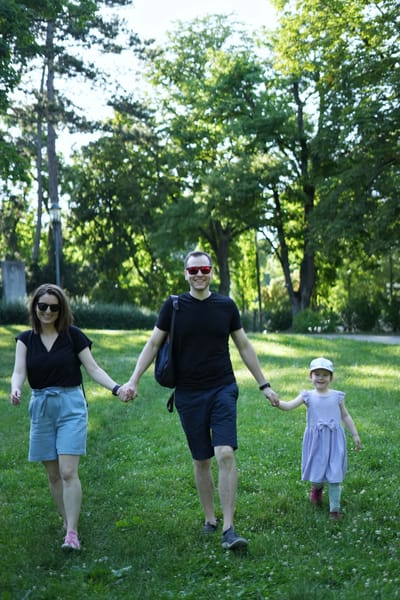 Family of three walking hand in hand through a sunny Vienna park
