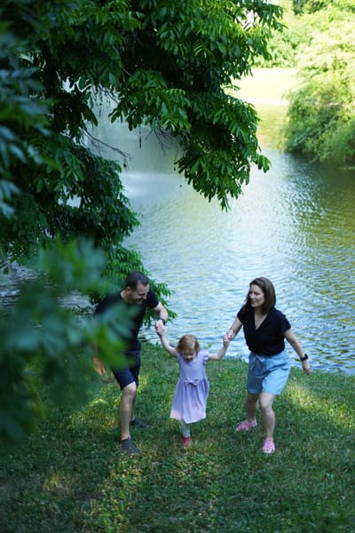 Parents swinging toddler daughter by the arms along a lakeside path