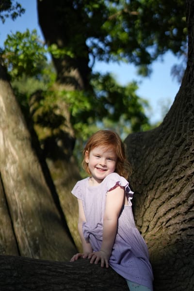 Red-haired girl smiling while climbing a large tree branch in a park