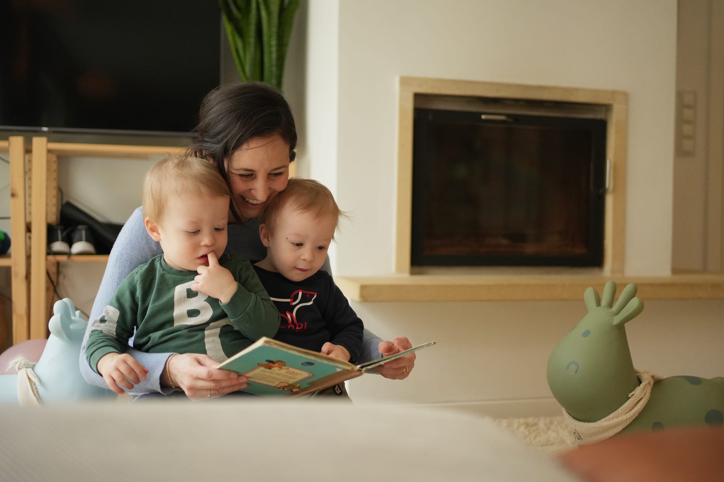 Mother reading a picture book to two toddlers cuddled on the sofa