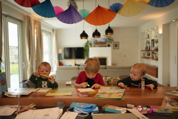 Three children side by side at the table with books and crayons, paper garlands overhead