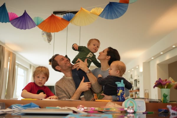 Family of five at the table, father lifting a toddler high with colorful garlands above