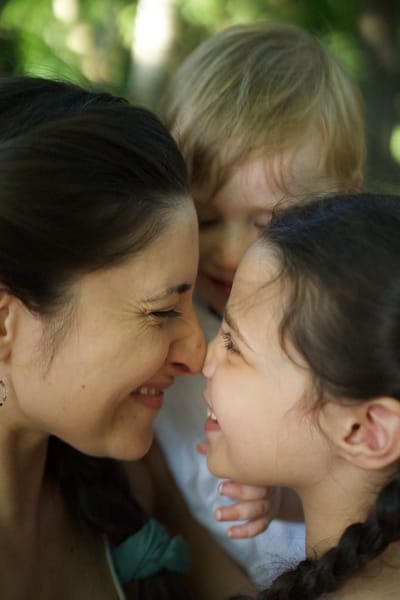 Mother and two children nose-to-nose, close-up with soft garden bokeh