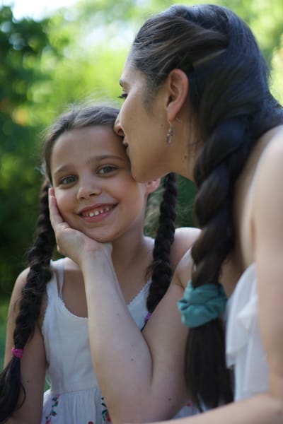 Mother kissing daughter on the cheek, girl with braids smiling at camera