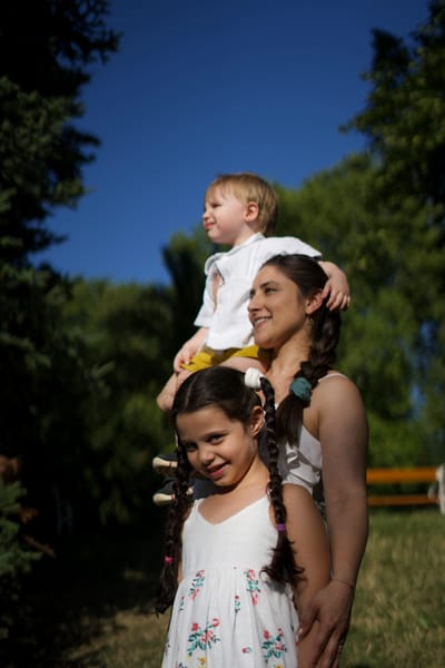 Mother with toddler on her shoulders and daughter in front, blue sky behind