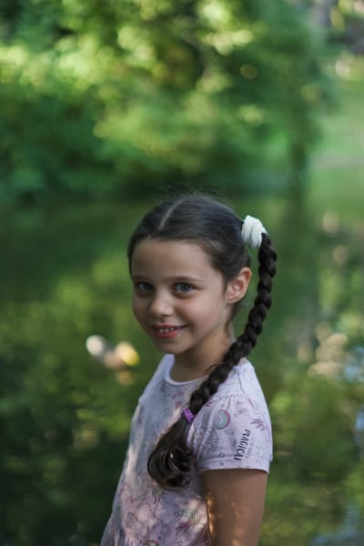 Girl with braided pigtails glancing over her shoulder in a lush green park