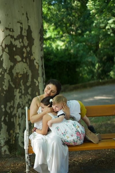 Mother and two children cuddling on a park bench under a plane tree
