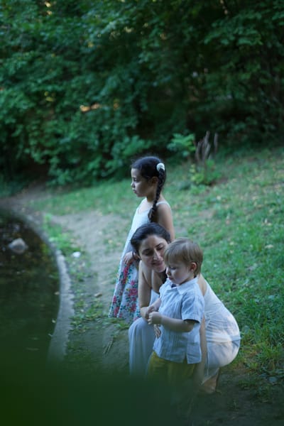 Mother crouching with daughter and toddler by a stream in a Vienna park