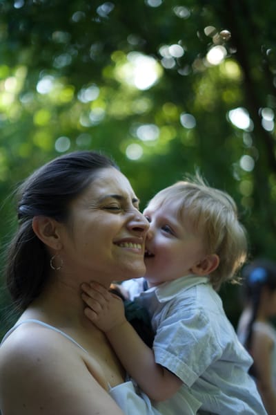 Mother and toddler son laughing cheek-to-cheek, garden greenery behind