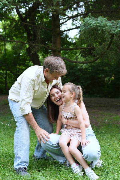 Father leaning over mother and daughter laughing together on park grass