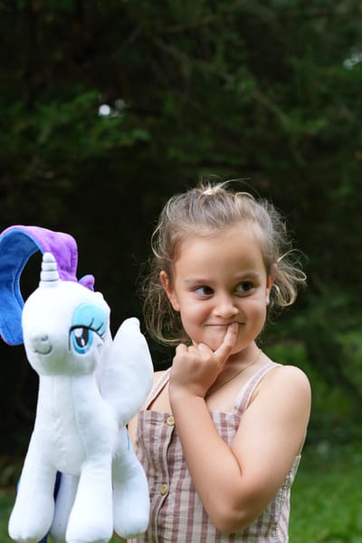 Young girl with a cheeky smile holding a unicorn plush toy in the garden
