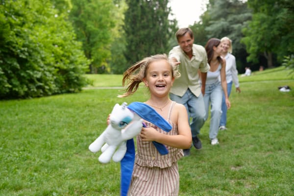 Girl running with a stuffed unicorn while parents chase her across a Vienna park