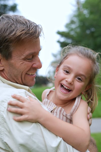 Father holding laughing daughter in his arms, close-up outdoor portrait