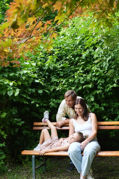 Family relaxing on a park bench, daughter lying across her parents laps