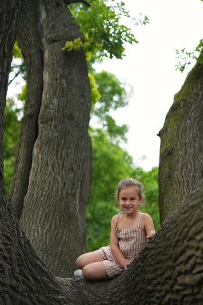 Smiling girl sitting in the fork of a large old tree in a Vienna park