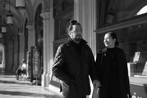 Couple walking side by side under the arcades, past a shop window