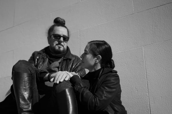 Couple sitting against a sunlit stone wall, her hand resting on his knee