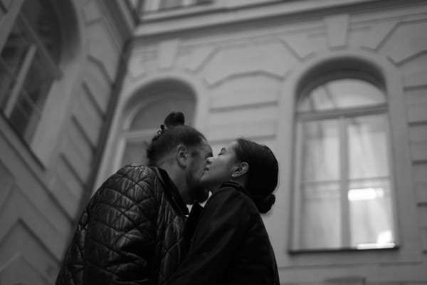 Couple kissing in a courtyard in front of tall arched windows