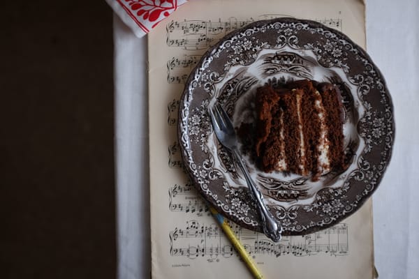 Slice of layered chocolate cake on a vintage transferware plate atop sheet music with silver fork