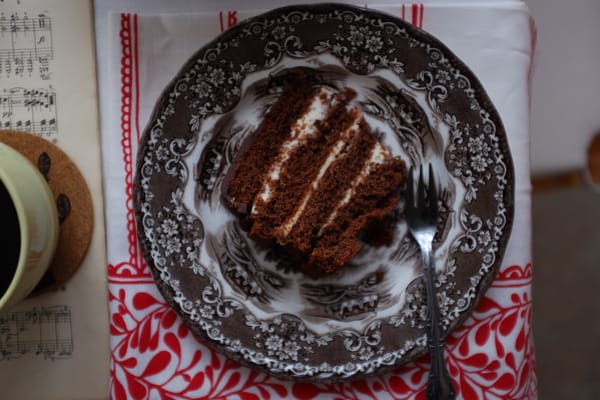 Close-up of four-layer chocolate cake slice on vintage plate with folk towel and black coffee