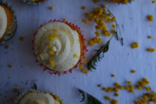 Close-up of a lemon cupcake in a pink liner with swirled frosting and zest, mimosa in soft focus
