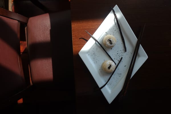 Two mochi dusted with dark crumbs on a white plate with vanilla pods in a warm cafe setting
