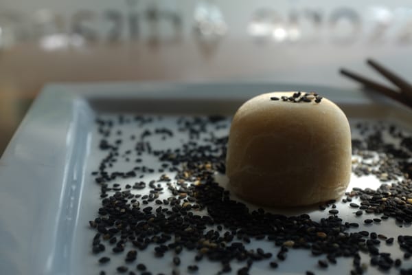 Close-up of golden mochi surrounded by scattered black sesame seeds on a white plate