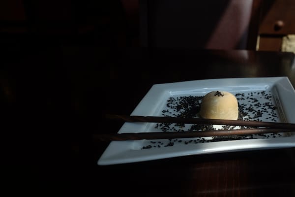 Single mochi on a white plate with vanilla pod, dramatic side lighting on dark wood table