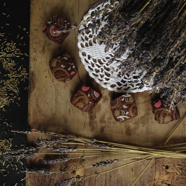 Square chocolate petit fours with gold and pink paisley prints on rustic wood with dried lavender