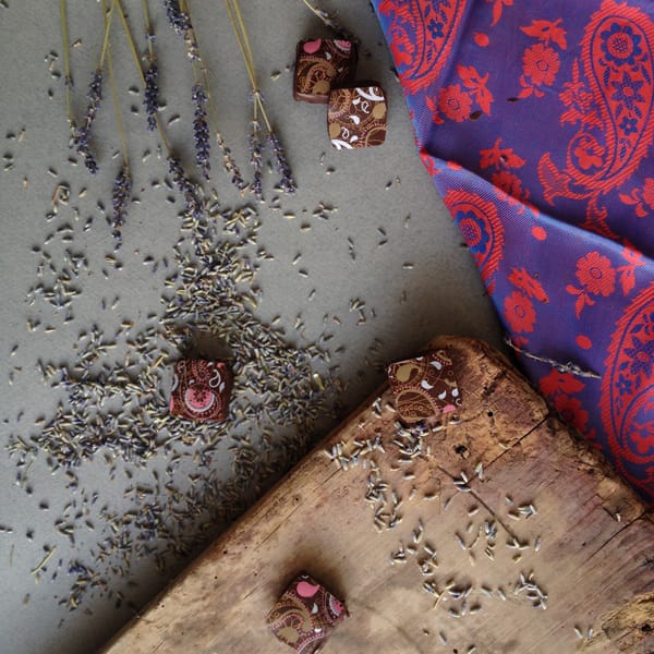 Three chocolate petit fours on worn wood and grey surface with scattered dried lavender buds