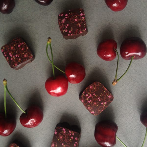 Chocolate petit fours with cherry blossom prints alongside glossy dark red cherries on grey surface