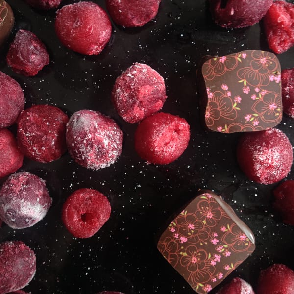 Frost-covered dark cherries and chocolate bonbons with floral prints on a black surface
