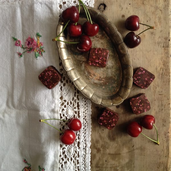 Petit fours and fresh cherries arranged around a vintage brass tray on linen and weathered wood