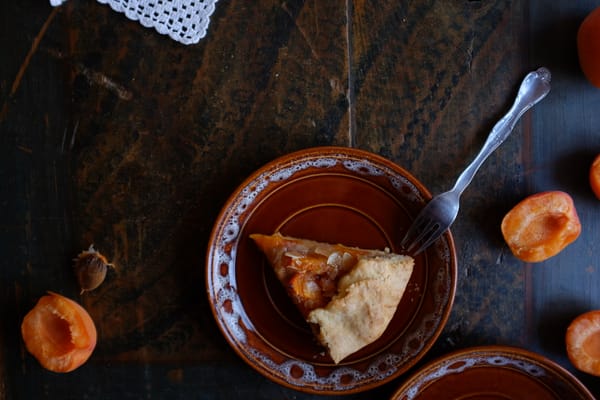 Apricot galette slice on stacked ceramic plates with halved apricots and crocheted doily on dark wood