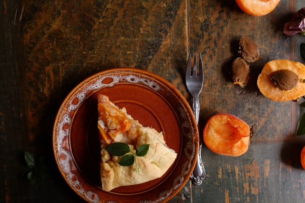 Galette slice with fresh mint garnish on brown plate, halved apricots and dried roses on painted wood