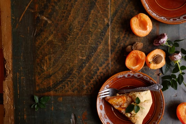 Apricot galette slice on ceramic plate with faded pink rose on heavily weathered blue-grey wood surface