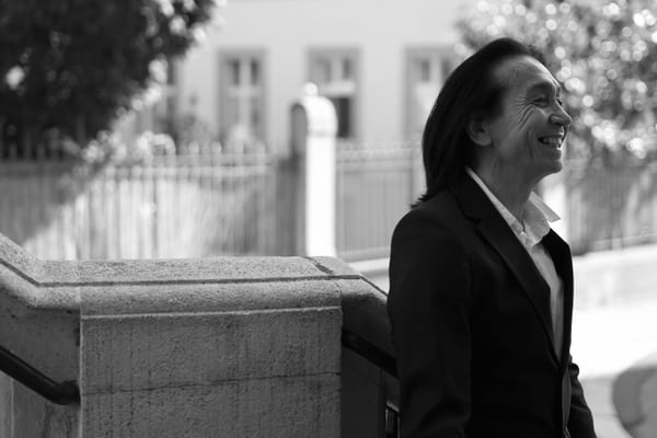 Man laughing in profile beside a stone wall, black and white