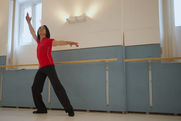 Dancer in a red shirt with one arm raised in a ballet studio with barres