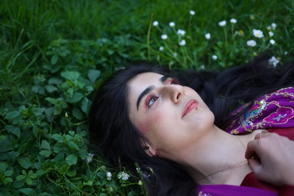 Woman in traditional robe lying on lush Vienna park grass among small white flowers, gazing upward