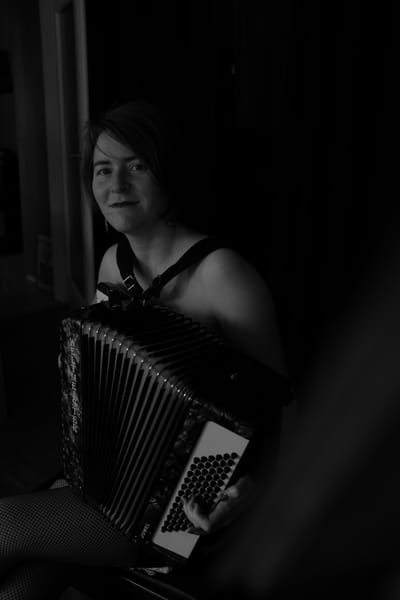 Black and white portrait of a woman playing a Weltmeister accordion by window light