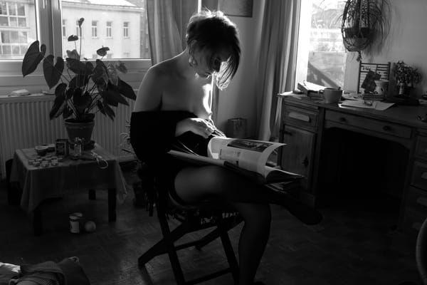 Woman seated by a window reading a magazine, black and white with natural daylight