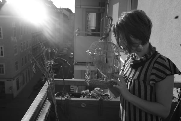 Woman on a Vienna balcony holding a decorative birdcage, black and white with sun flare