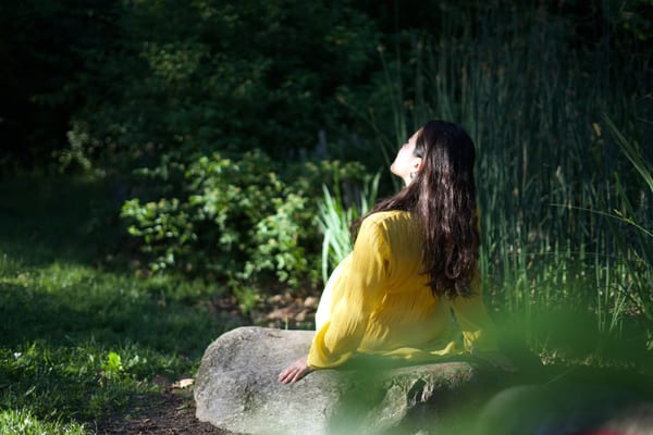 Woman in yellow sitting on a rock with her face turned up to the sun