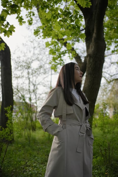 Woman in light neutral coat gazing upward among Vienna park trees